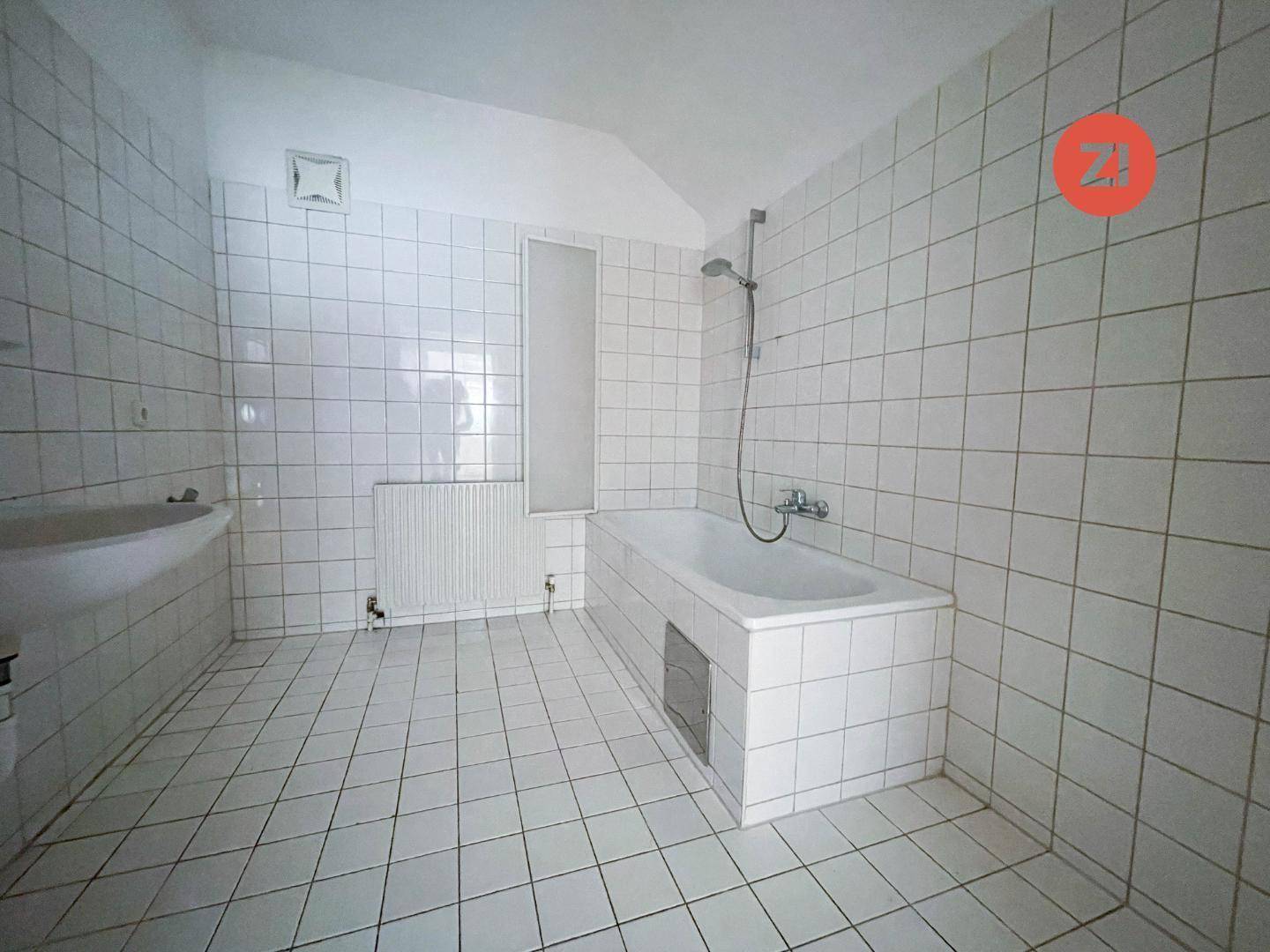 Gefliestes Badezimmer mit Badewanne, Duschfunktion und Heizkörper.