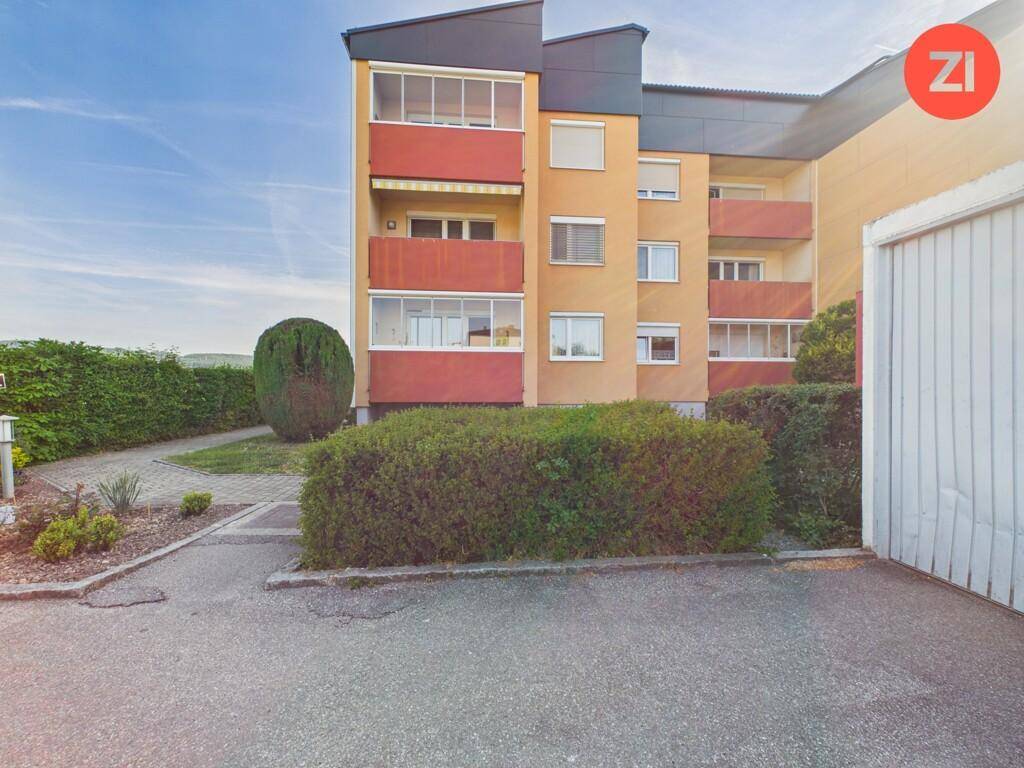 Mehrfamilienhaus mit Balkonen, umgeben von Hecken und Grünflächen.