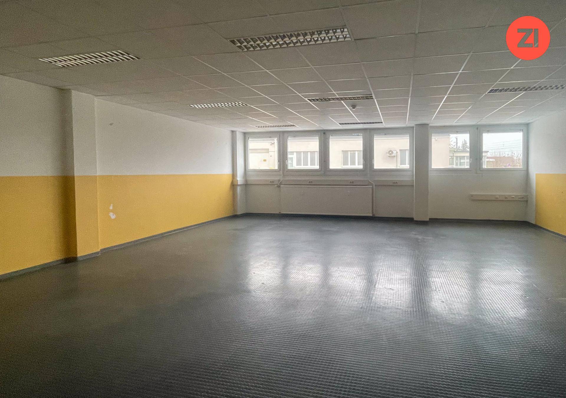 Großes, leeres Büro mit gelb-weißen Wänden, vielen Fenstern und einer abgehängten Gitterdecke.