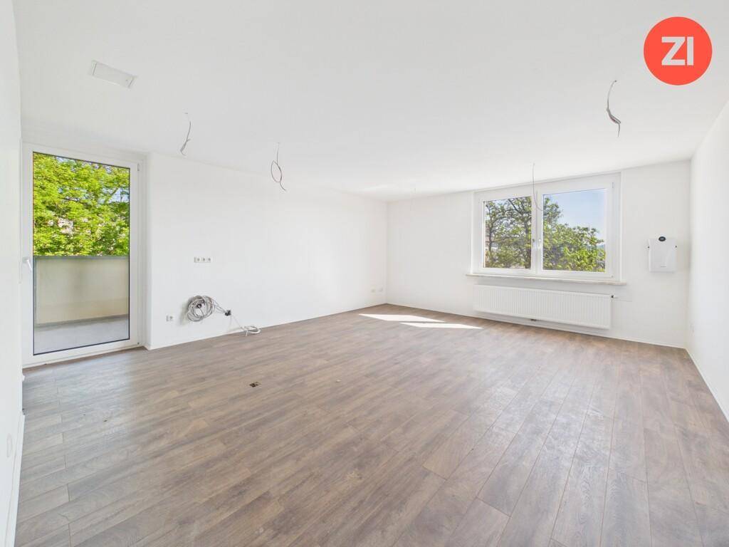 Geräumiges, helles Wohnzimmer mit Holzboden, großen Fenstern und Zugang zum Balkon.