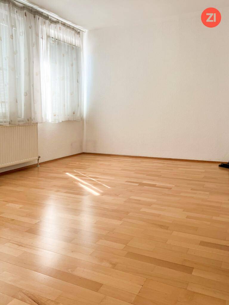 Geräumiges Zimmer mit hellem Holzfußboden und großen Fenstern, die viel Tageslicht hereinlassen.