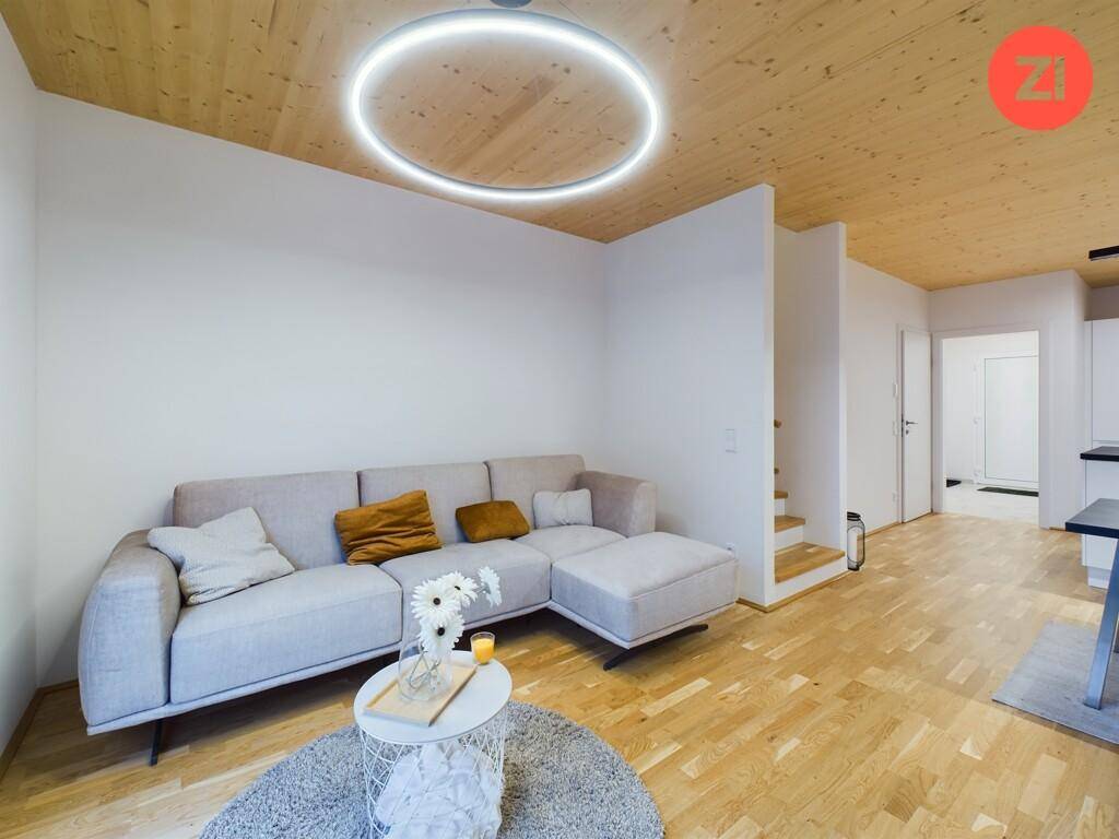 Gemütliches Wohnzimmer mit hellem Sofa, Holzboden und moderner Deckenbeleuchtung.