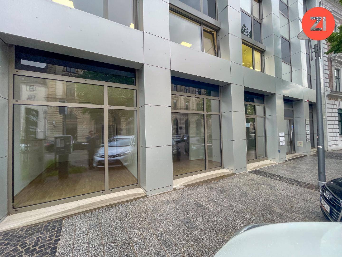 Moderne Geschäftsfassade mit großen Schaufenstern und reflektierenden Glasflächen an einer belebten Straße.
