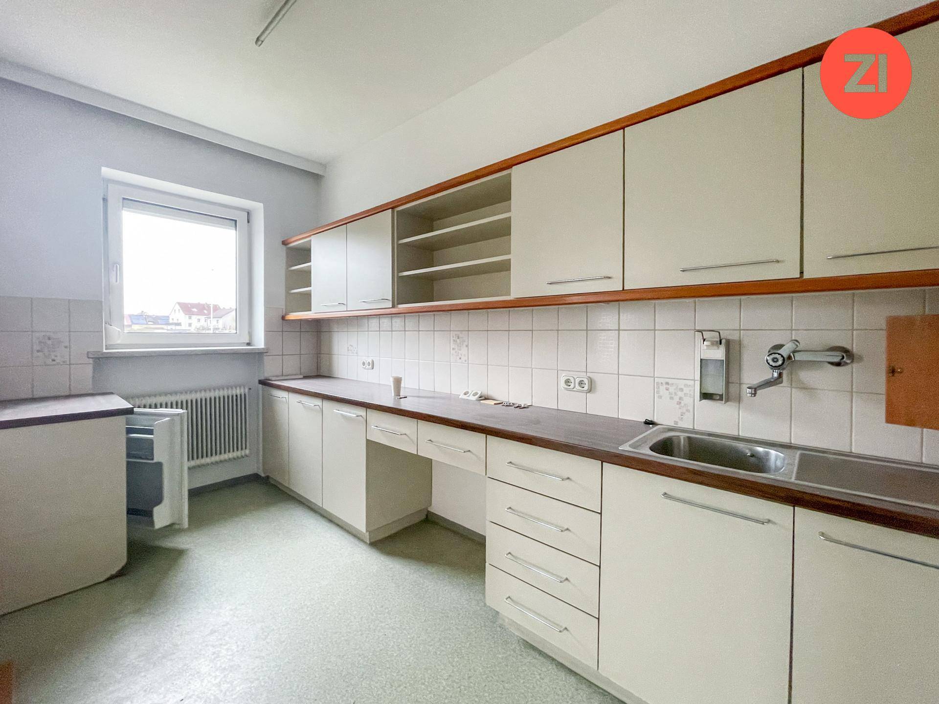 Funktionale Küche mit älteren Einbauschränken, Spüle und Fenster, bereit zur Modernisierung.