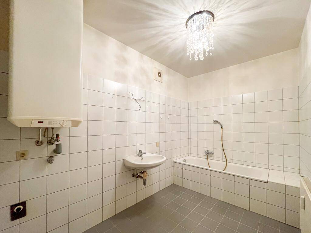 Gefliestes Badezimmer mit Badewanne, Waschbecken und einem Boiler an der Wand.