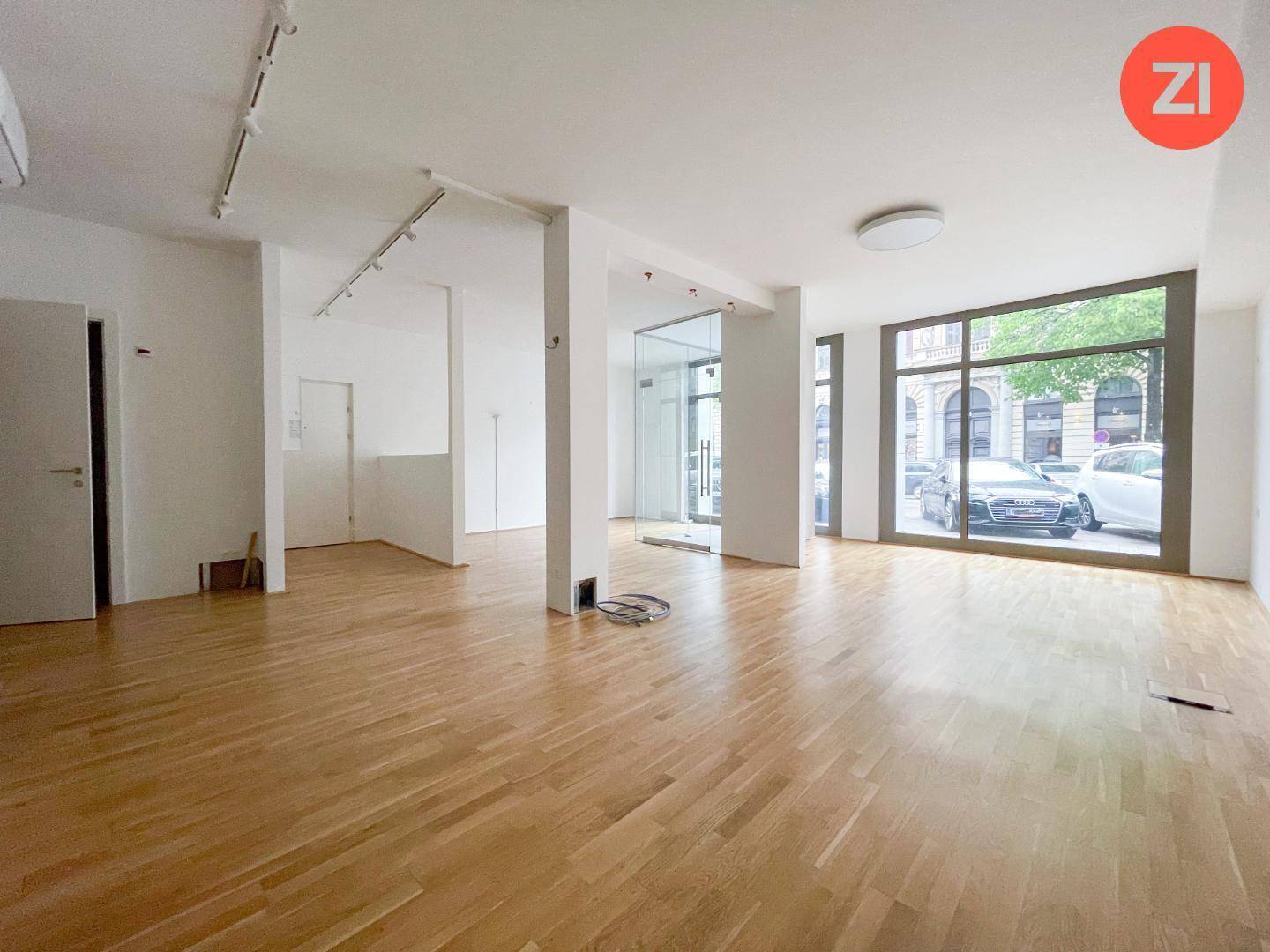 Großer, leerer Gewerberaum mit Holzboden, weißen Wänden und einer Klimaanlage an der Decke.