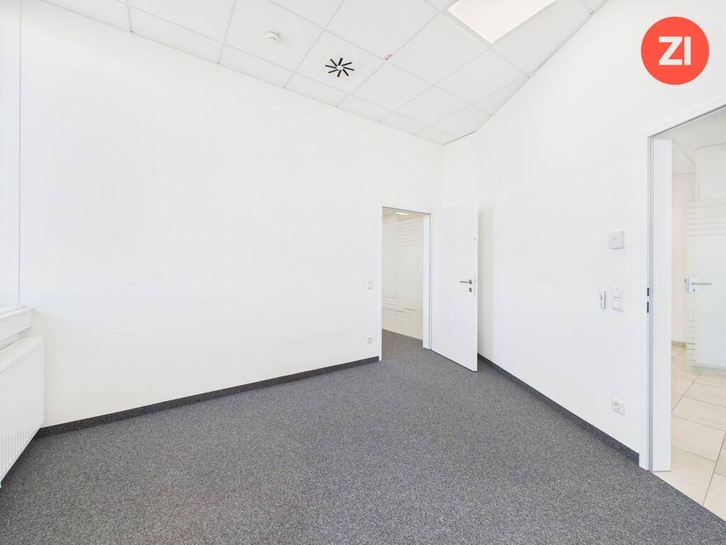 Leeres Büro mit Teppichboden, weißen Wänden und Zugang zu weiteren Räumen.
