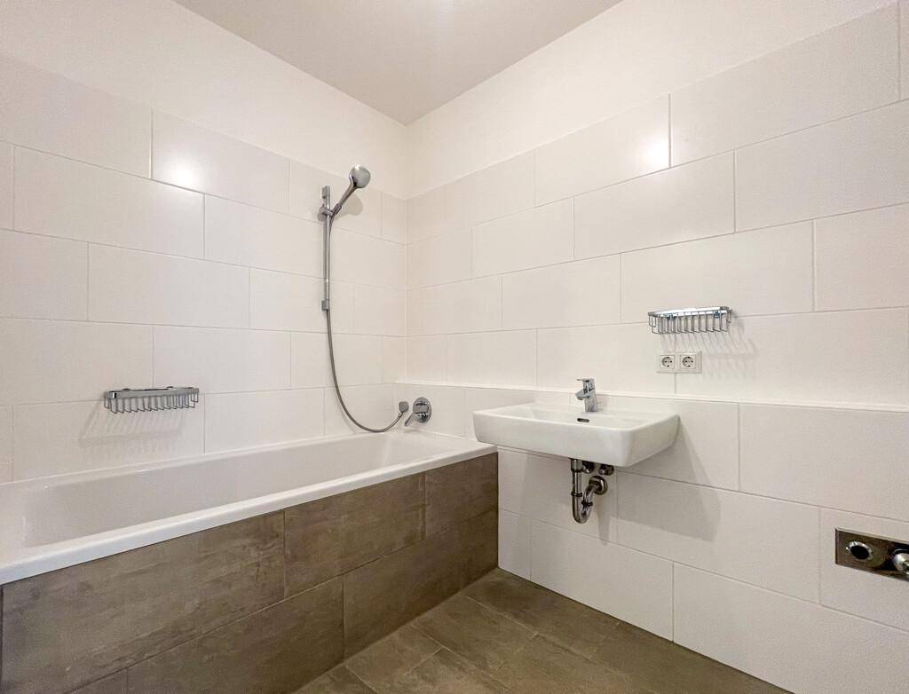Helles Badezimmer mit Badewanne, Waschbecken und modernen Fliesen.