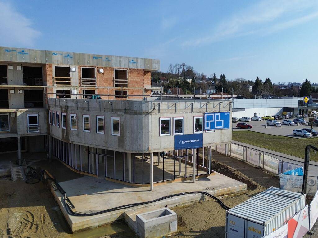 Fortgeschrittene Baustelle eines modernen Gebäudes mit Betonstrukturen, großen Fenstern und Glasfassade im Erdgeschoss.