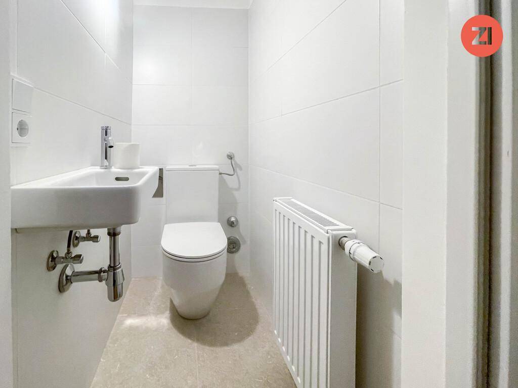 Kompaktes Gäste-WC mit modernem WC, kleinem Waschbecken und einem Heizkörper an der Wand.
