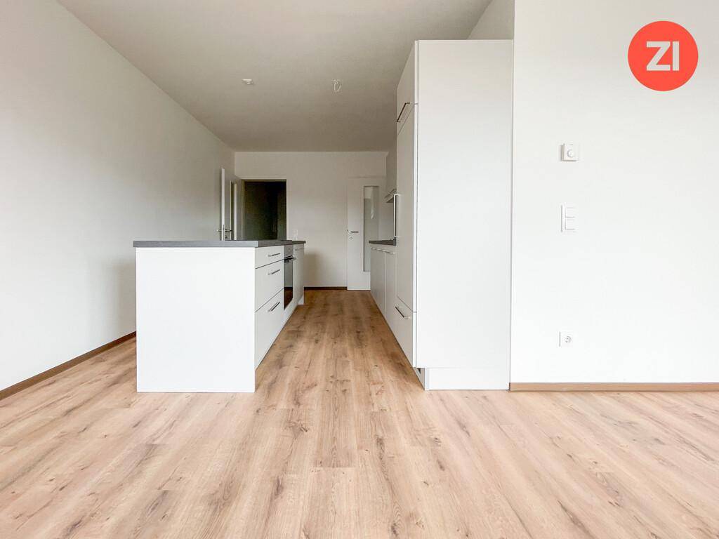 Heller, offener Küchenbereich mit Kücheninsel und Laminatboden, der in den Wohnraum übergeht.