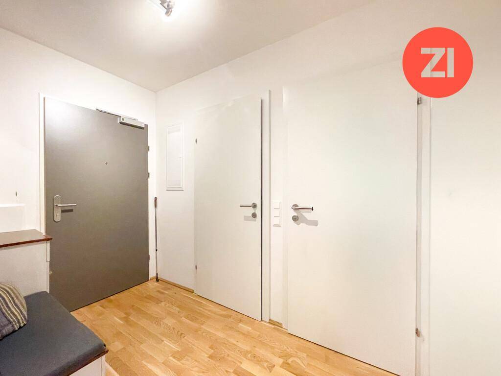 Eingangsbereich der Wohnung mit Holzboden, weißer Tür und Sitzgelegenheit.