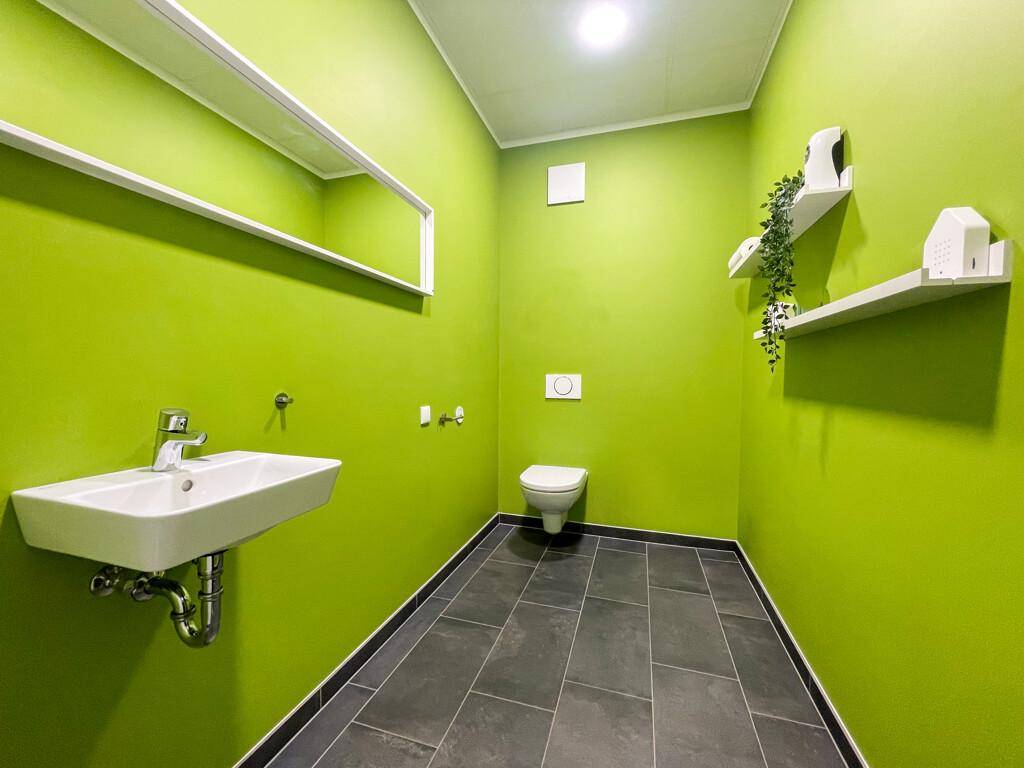 Modernes WC mit leuchtend grünen Wänden, dunklen Fliesen und einem wandhängenden WC und Waschbecken.