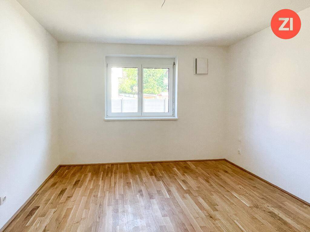 Weiteres helles Schlafzimmer mit Eichenparkettboden und einem Fenster für natürliche Belichtung.