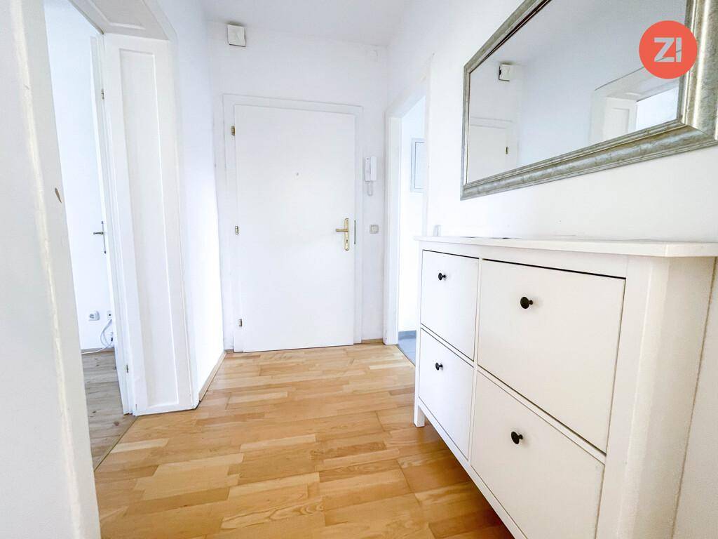 Freundlicher Eingangsbereich mit Holzboden, Schuhschrank und einem großen Wandspiegel.