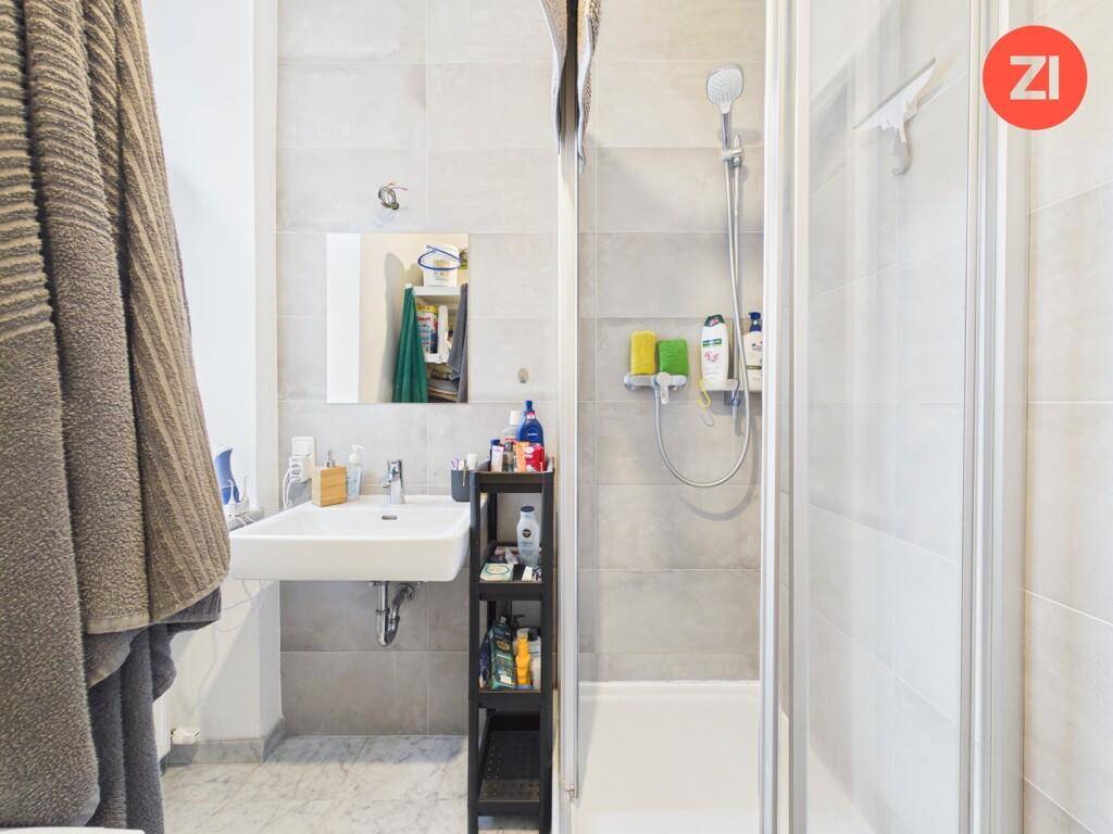 Helles Badezimmer mit Duschkabine, Waschbecken und modernen grauen Fliesen.