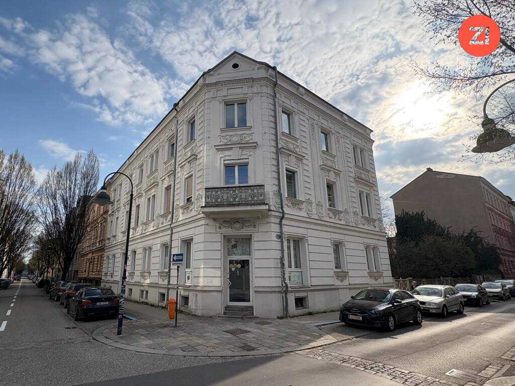 Eckgebäude mit weißer Fassade und dekorativen Elementen an einer belebten Stadtstraße.