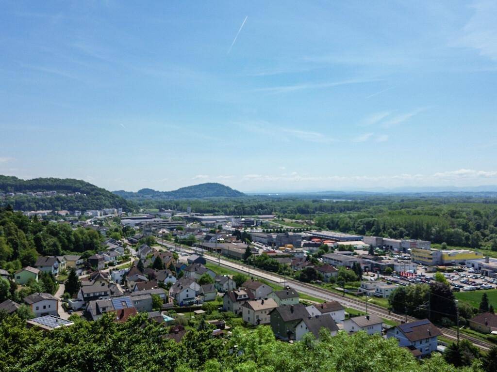 Blick auf eine gemischte Wohn- und Gewerbezone mit Verkehrswegen und grünen Hügeln im Hintergrund.