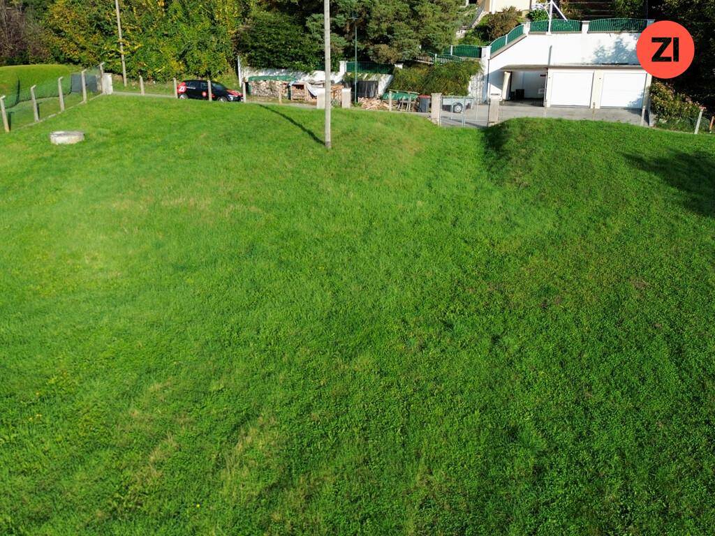 Grüne Wiese mit leichtem Gefälle und Blick auf ein Haus mit Garagen im Hintergrund.