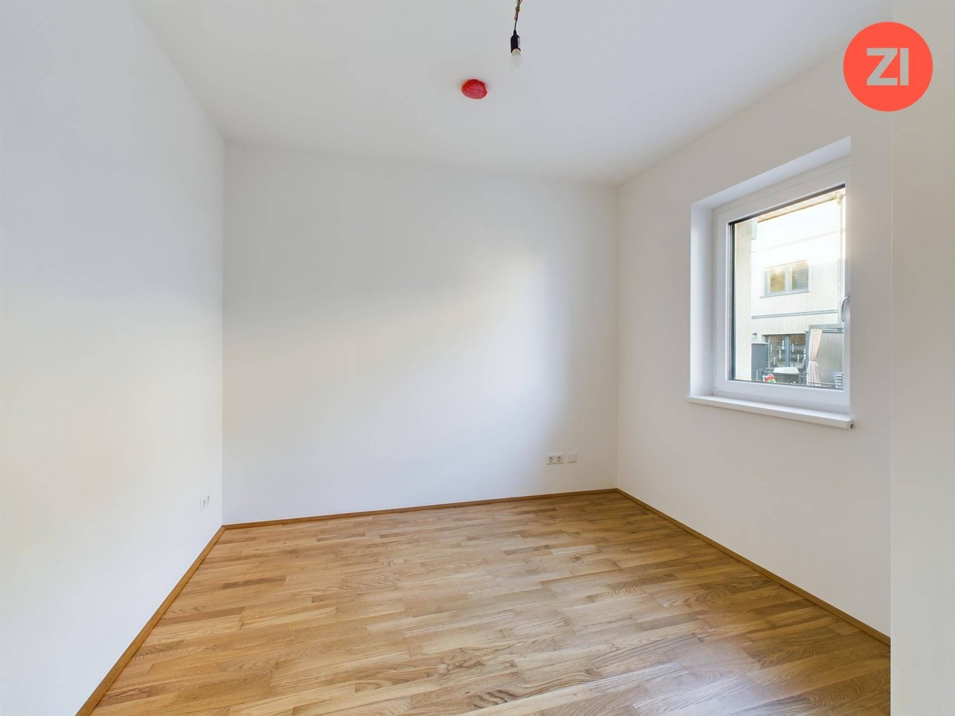 Helles, leeres Zimmer mit Parkettboden und einem großen Fenster, das viel Tageslicht bietet.