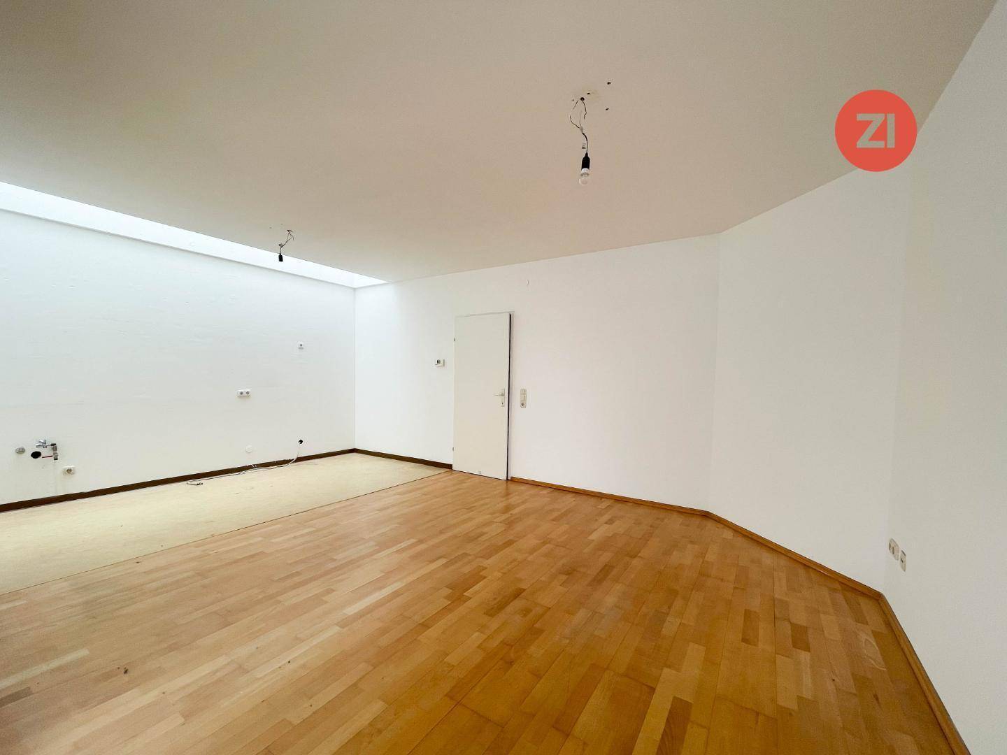 Großes, leeres Zimmer mit Parkettboden und weiß gestrichenen Wänden, bereit zur individuellen Gestaltung.