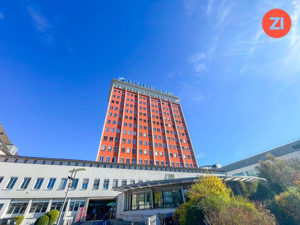 Hohes Bürogebäude mit markanter orangeroter Fassade und blauer Beschriftung unter strahlend blauem Himmel.