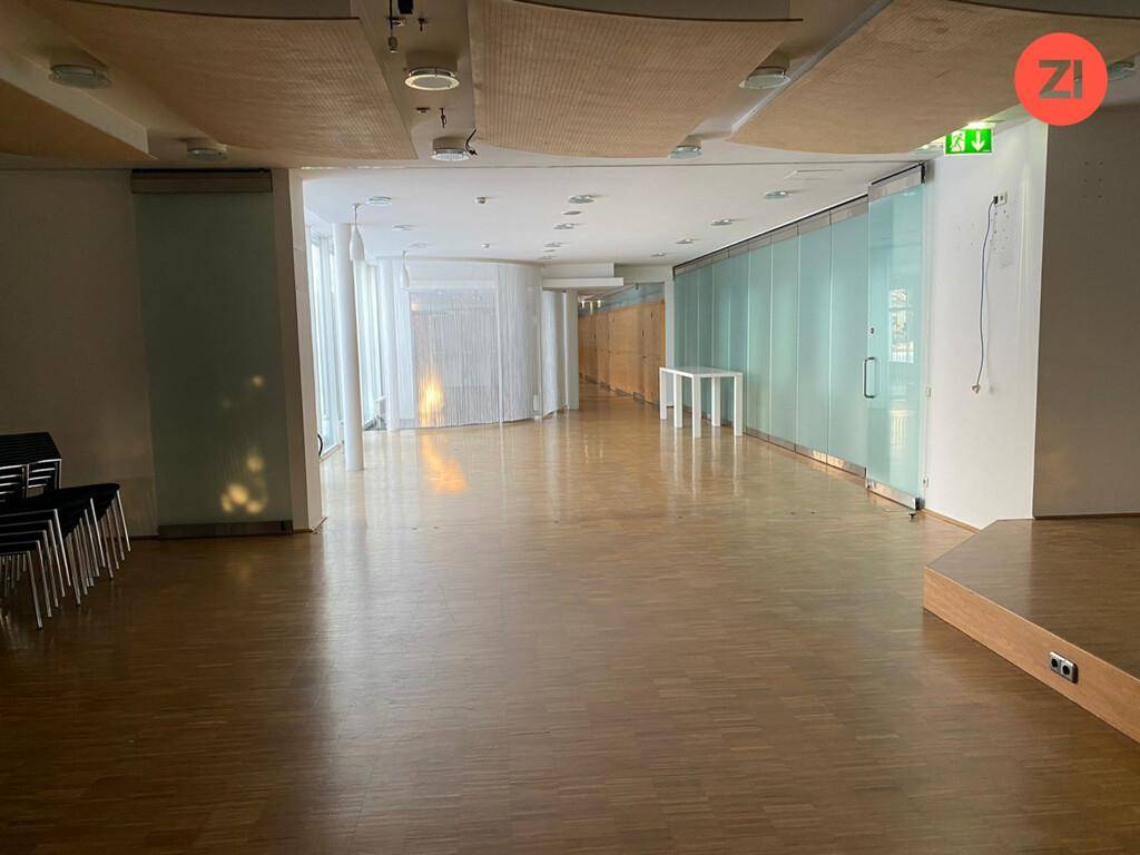 Geräumiger Konferenzbereich mit Holzboden, Glaswänden und viel Tageslicht, ideal für Veranstaltungen.