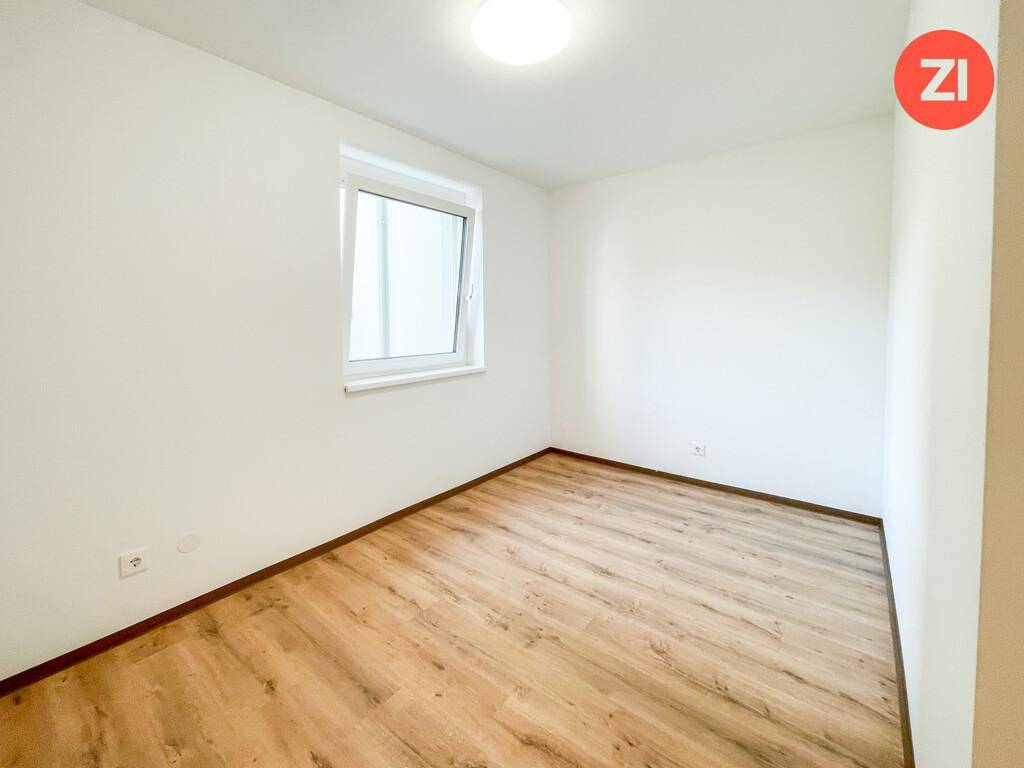 Helles Schlafzimmer mit Laminatboden und einem Fenster, das viel Tageslicht hereinlässt.