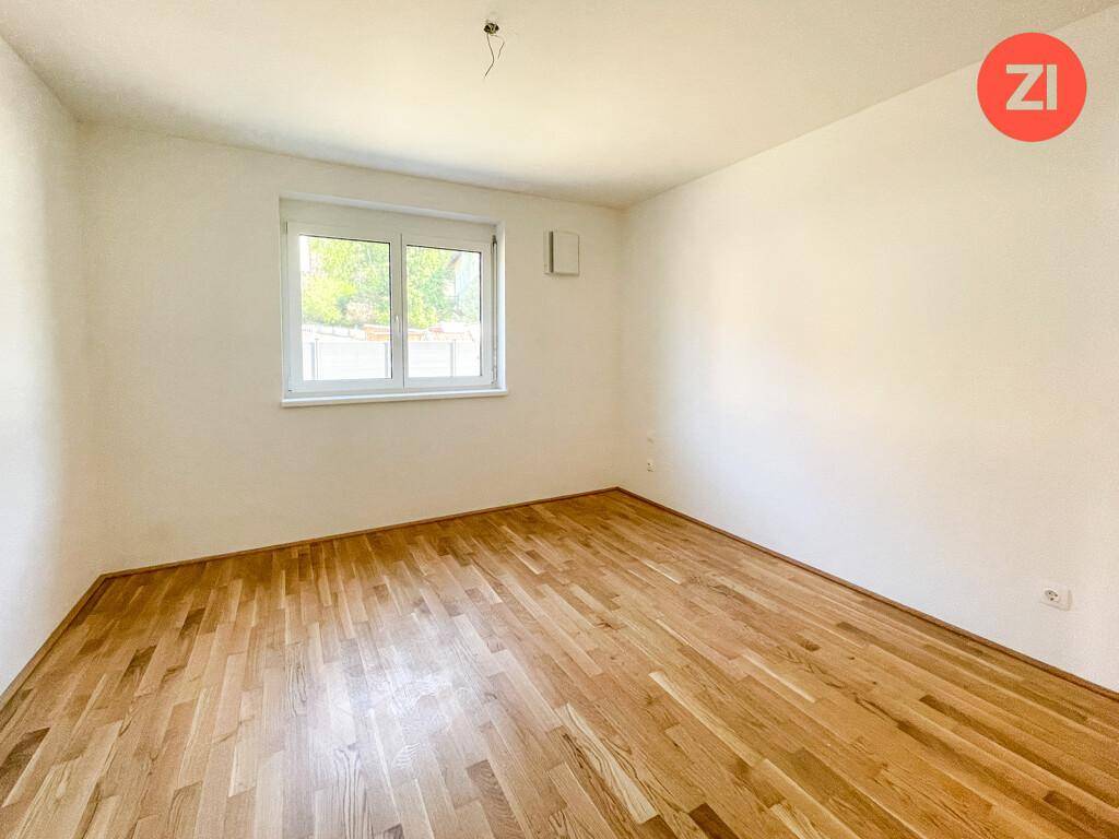Helles Schlafzimmer mit Eichenparkettboden und einem Fenster, das viel Tageslicht hereinlässt.