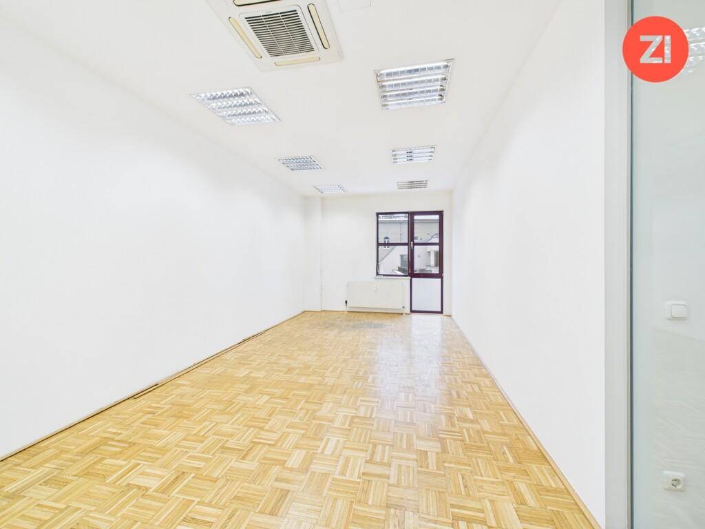 Länglicher Bürobereich mit Parkettboden und einem Fenster am Ende, das für natürliche Belüftung und Licht sorgt.