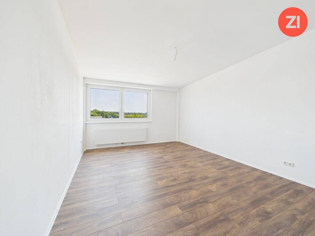 Leeres Schlafzimmer mit Laminatboden, großen Fenstern und weitem Blick ins Grüne.