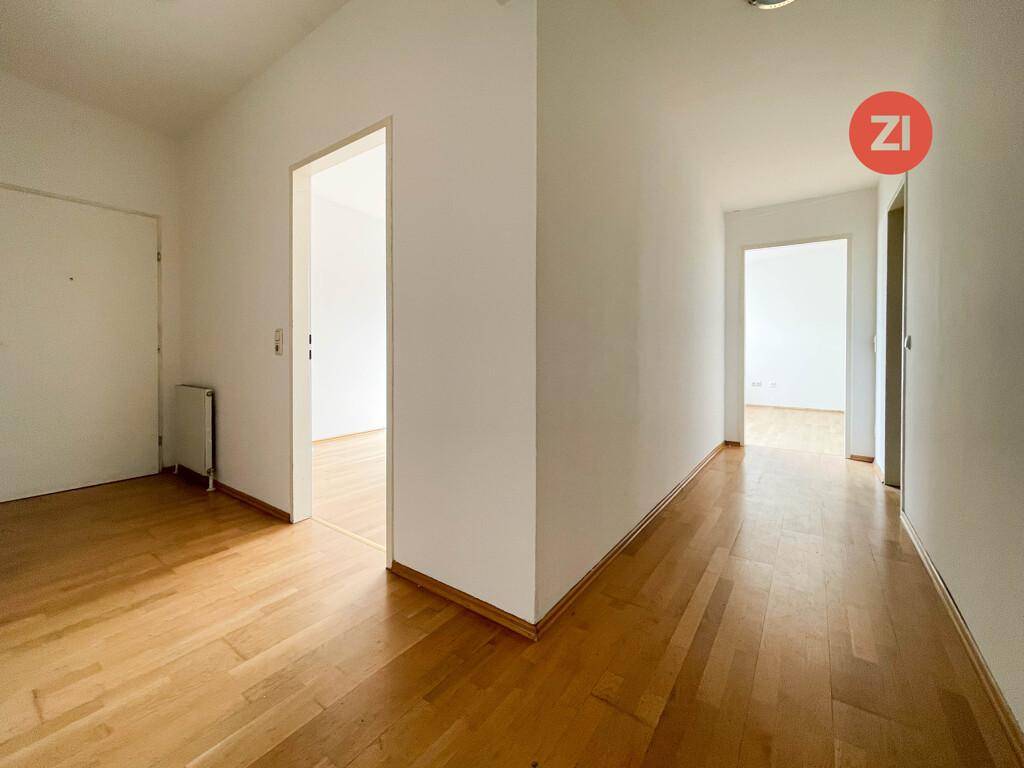 Heller Flur mit warmem Holzparkettboden und weißen Wänden, der zu verschiedenen Räumen führt.