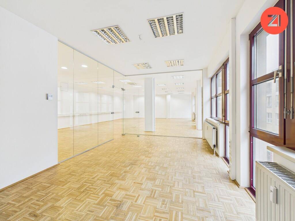 Teilansicht eines Büros mit reflektierenden Glaswänden, hellen Fenstern und Heizkörpern, die eine angenehme Arbeitsatmosphäre schaffen.