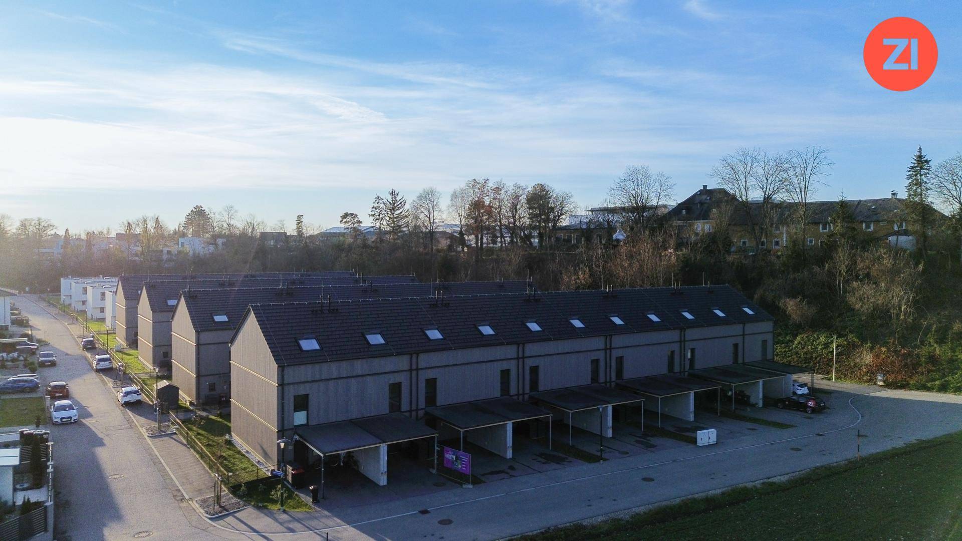 Weitläufige Ansicht einer modernen Reihenhaussiedlung mit Carports und grüner Umgebung.
