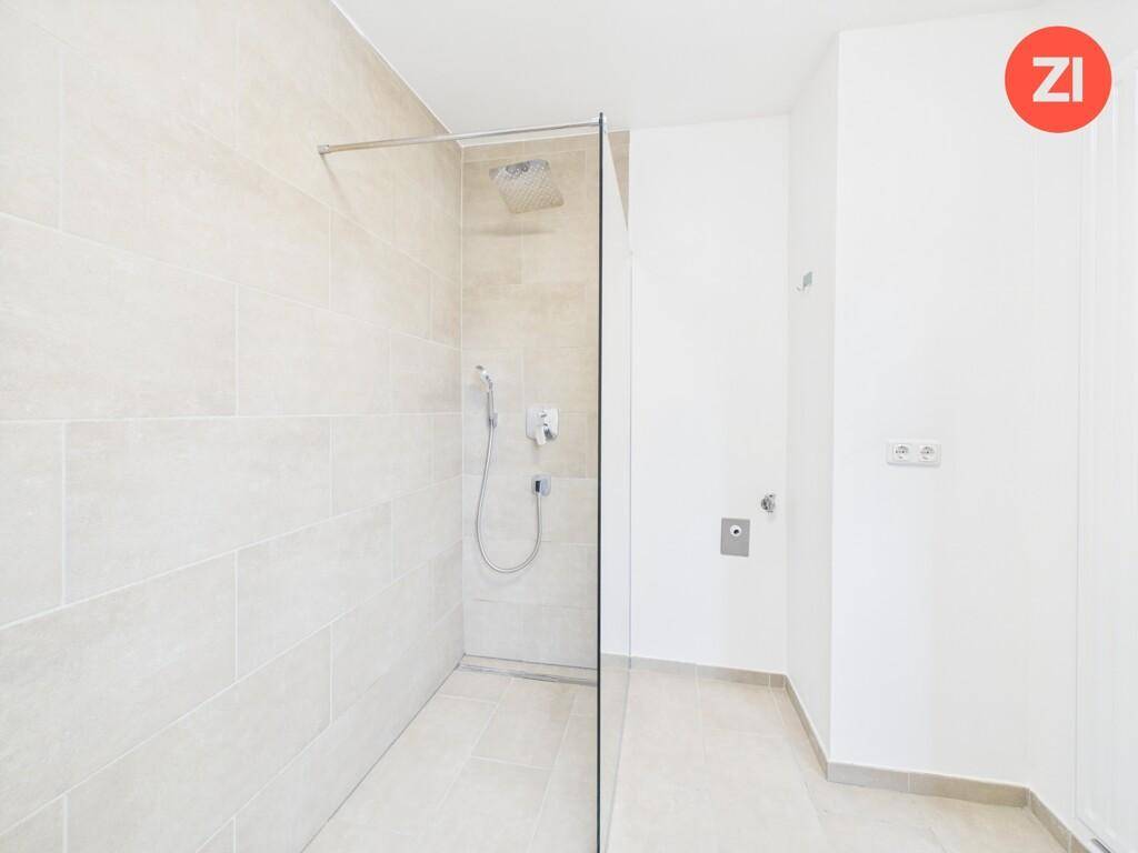 Geräumige, ebenerdige Dusche mit Glasabtrennung in einem hell gefliesten Badezimmer.