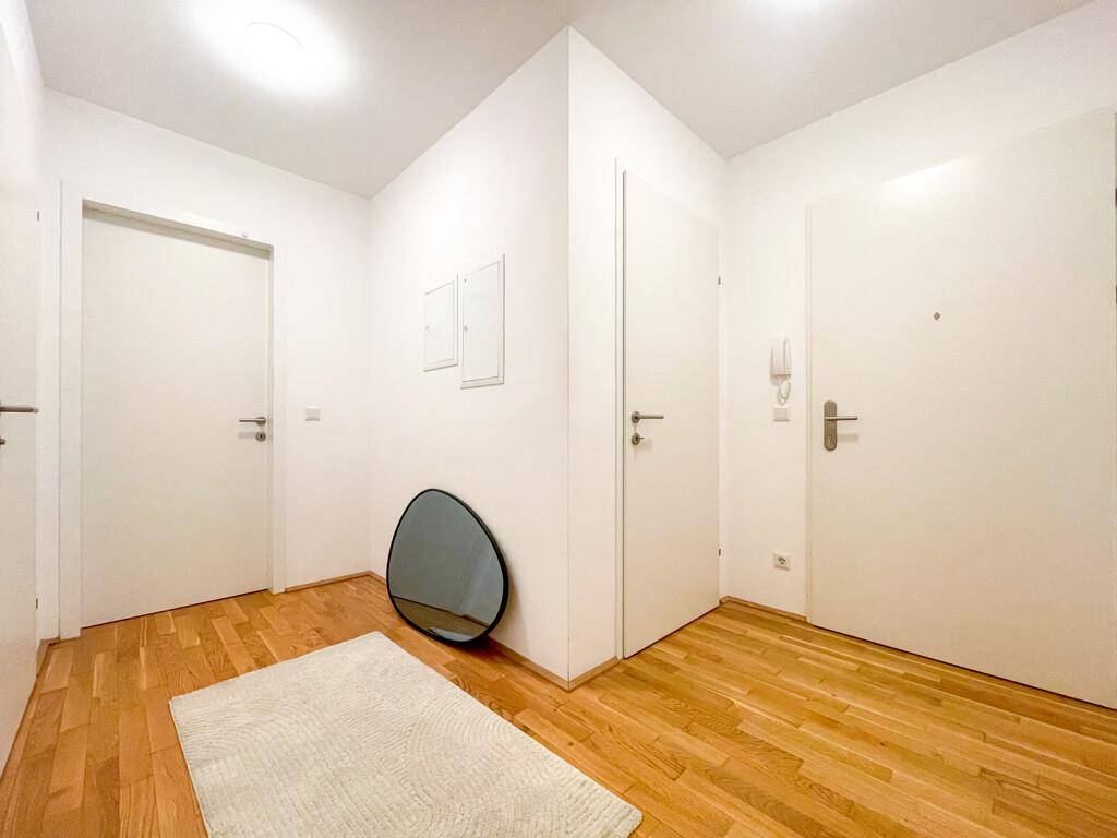 Heller Eingangsbereich mit Holzparkettboden, mehreren Türen und einem modernen Spiegel.