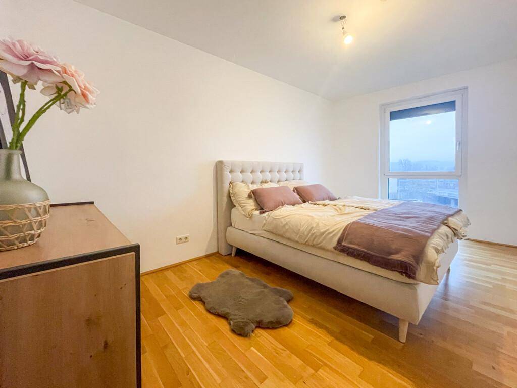 Helles Schlafzimmer mit Holzboden, großem Fenster und einem bequemen Doppelbett.