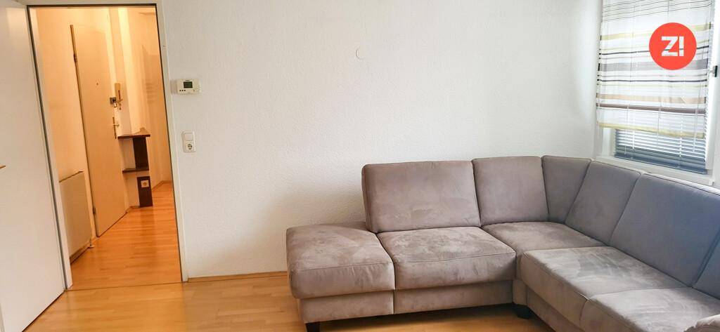 Gemütliches Wohnzimmer mit einem großen grauen Ecksofa, hellem Holzfußboden und Fenster.
