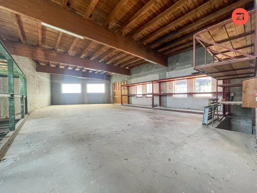 Großer Lagerraum mit Betonboden, sichtbaren Holzbalken und Regalsystemen, ideal für industrielle Nutzung.