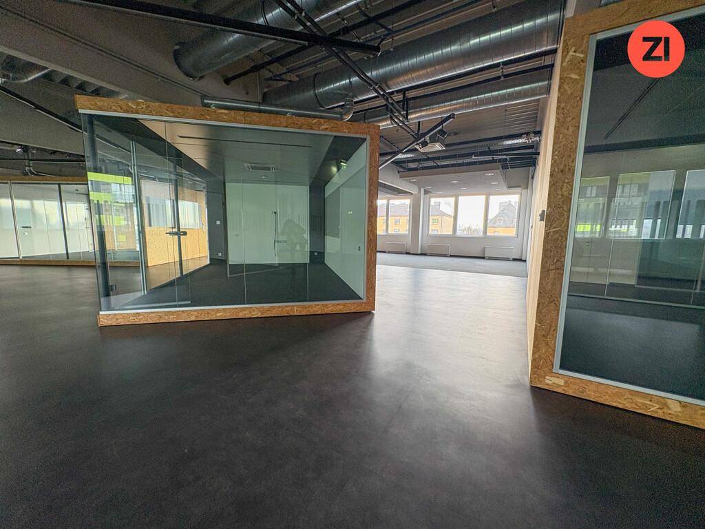 Offener Bürobereich mit freistehenden Glasboxen und Blick auf die Stadt durch große Fenster.