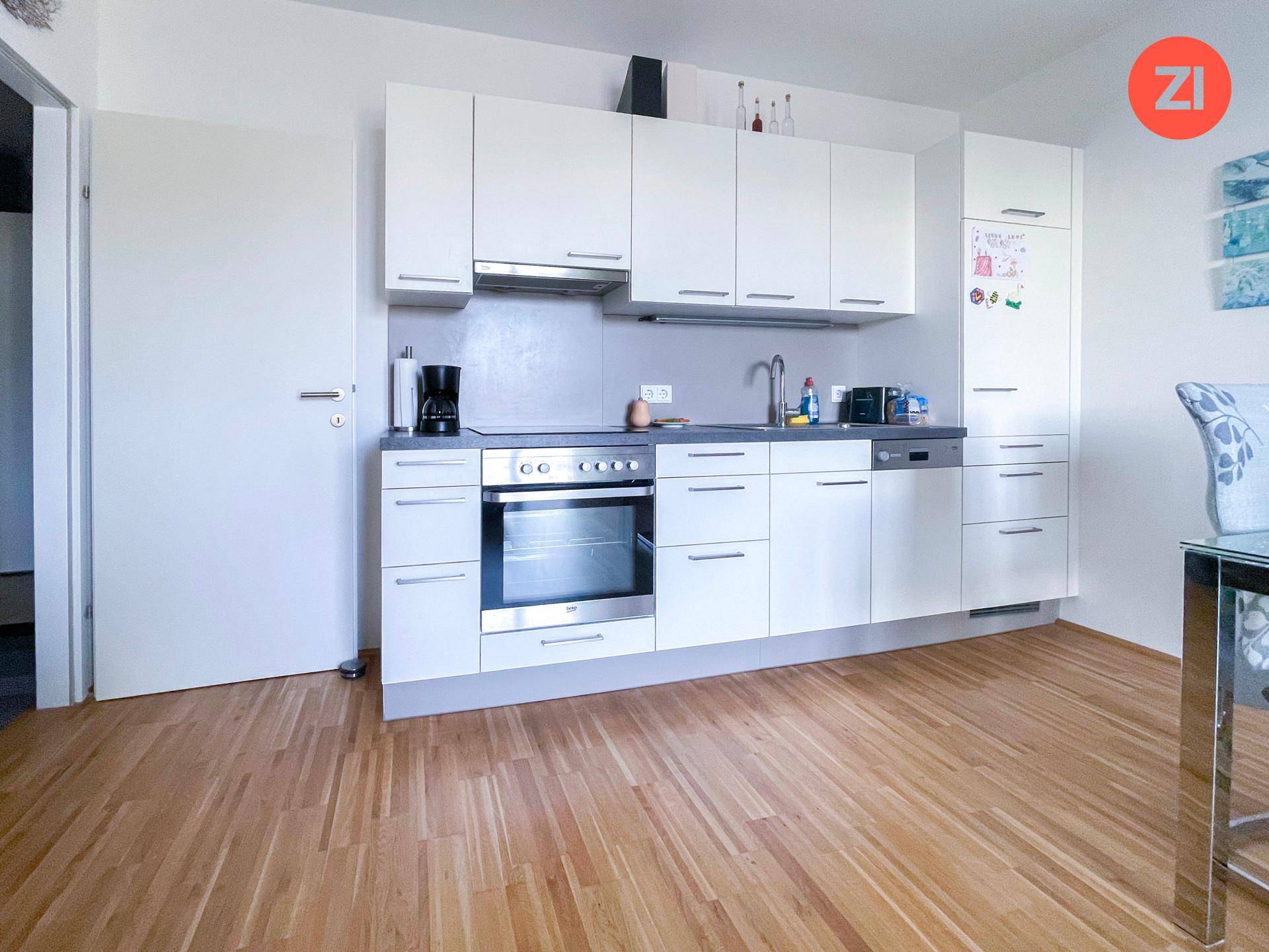 Moderne Einbauküche in Weiß mit integrierten Geräten und hellem Holzfußboden.
