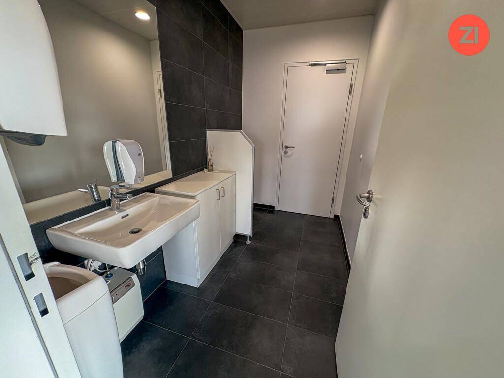 Modernes Badezimmer mit Waschbecken, Spiegel und dunklen Fliesen an der Wand und auf dem Boden.