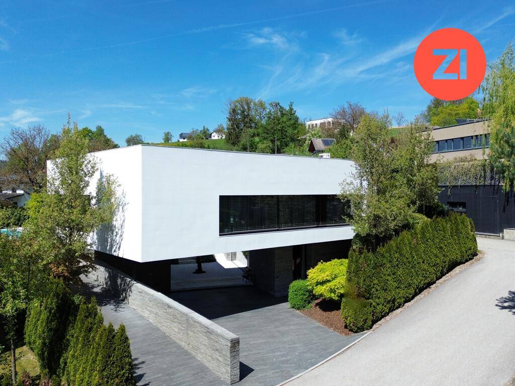 Elegantes, modernes Gebäude mit klaren Linien und einer Zufahrt, umgeben von gepflegten Hecken.