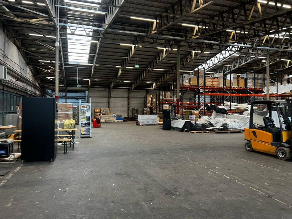 Geräumige Lagerhalle mit viel freiem Platz, einigen Waren und einem Gabelstapler im Hintergrund.