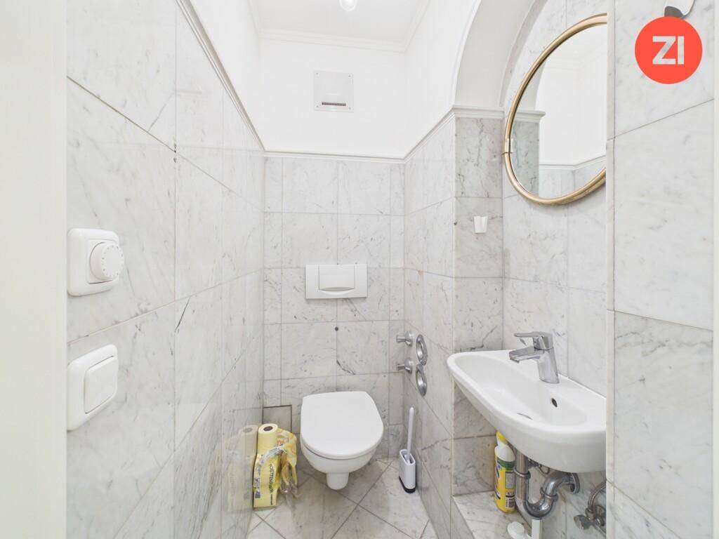 Elegantes Gäste-WC mit Marmorfliesen, wandhängendem WC und einem stilvollen runden Spiegel.