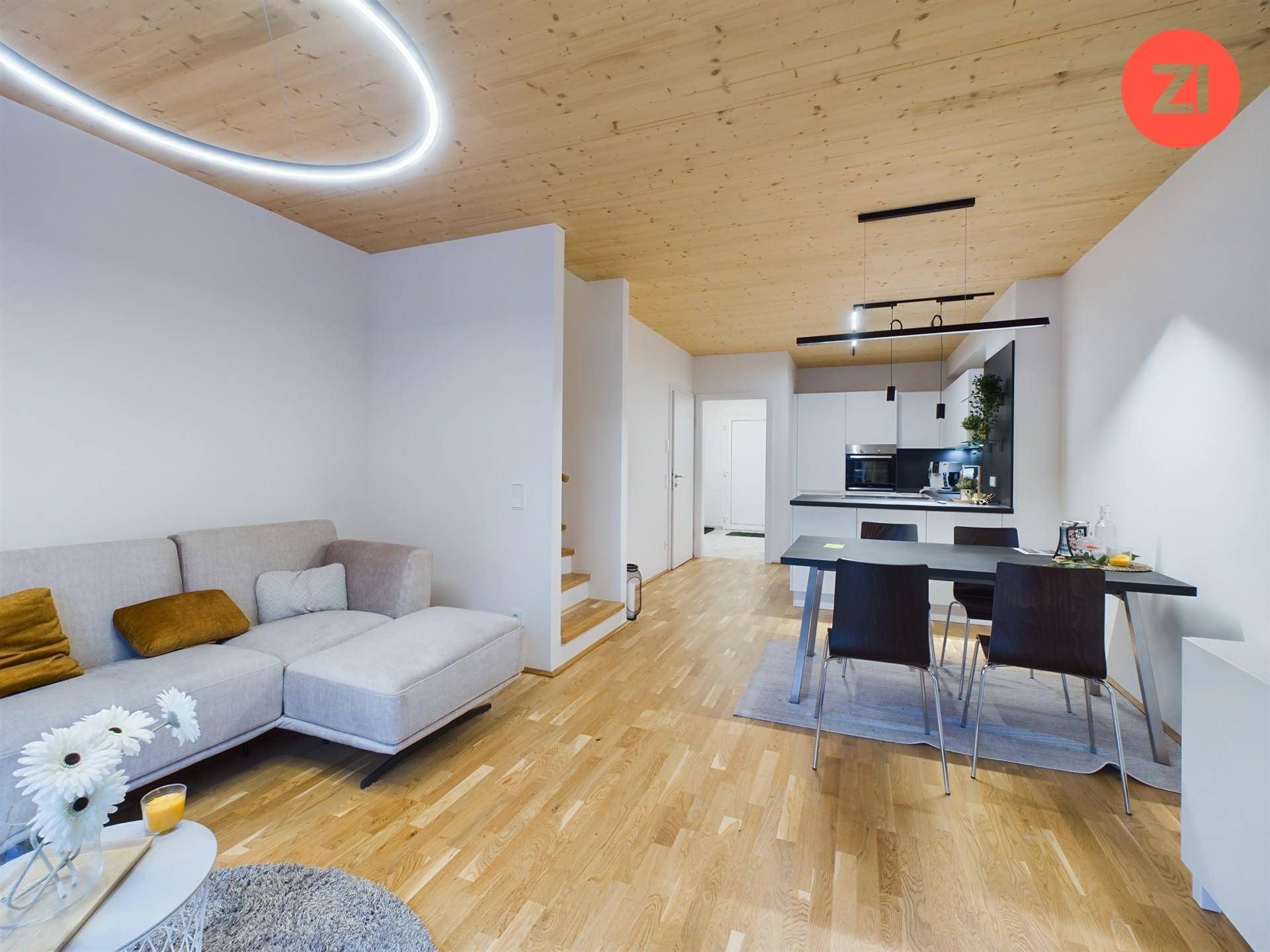 Geräumiger offener Wohnbereich mit Küche, Essbereich und Sofa, alles unter einer Holzdecke.