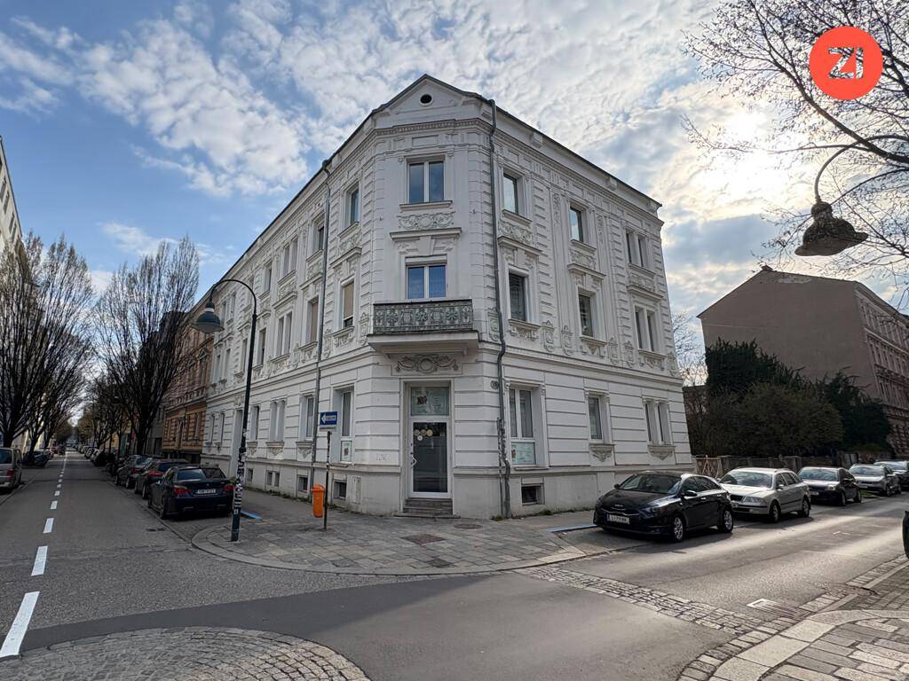 Weißes Eckgebäude mit klassischer Fassade und Balkon an einer städtischen Straße.