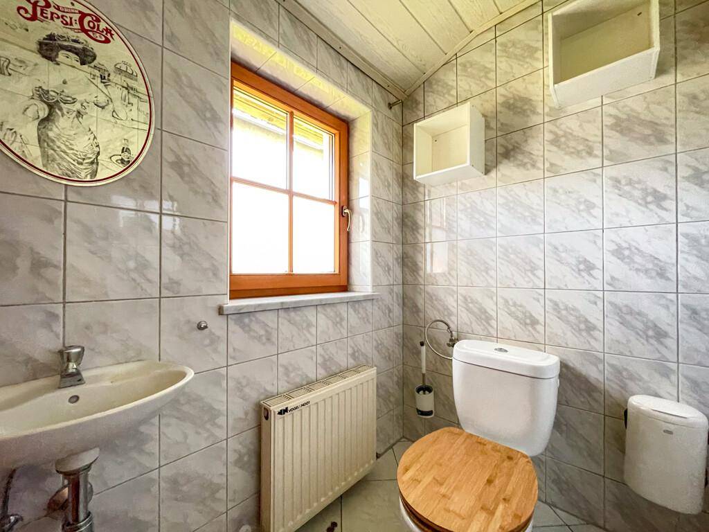 Kleines Gäste-WC mit hellen Fliesen, Holzfenster und einem Heizkörper.