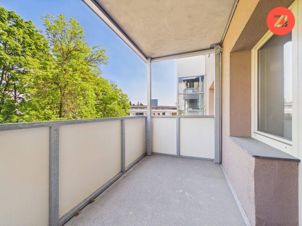Moderner Balkon mit Glasbrüstung und Blick auf Bäume und die Umgebung.
