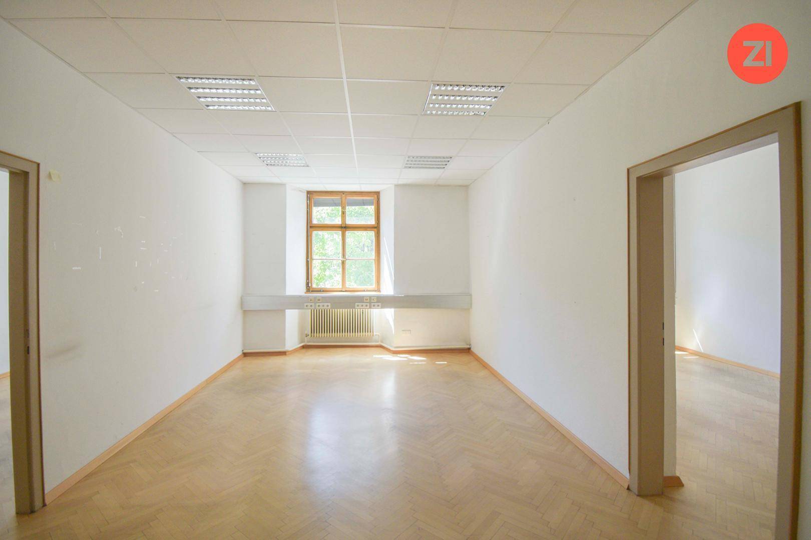 Helles Büro mit Fischgrätparkett, großem Fenster und zwei Türen, vielseitig nutzbar und einladend.